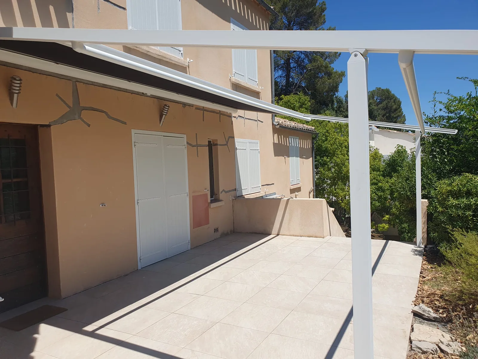 Structure de pergola blanche fixée à la maison, vue latérale sur la terrasse.