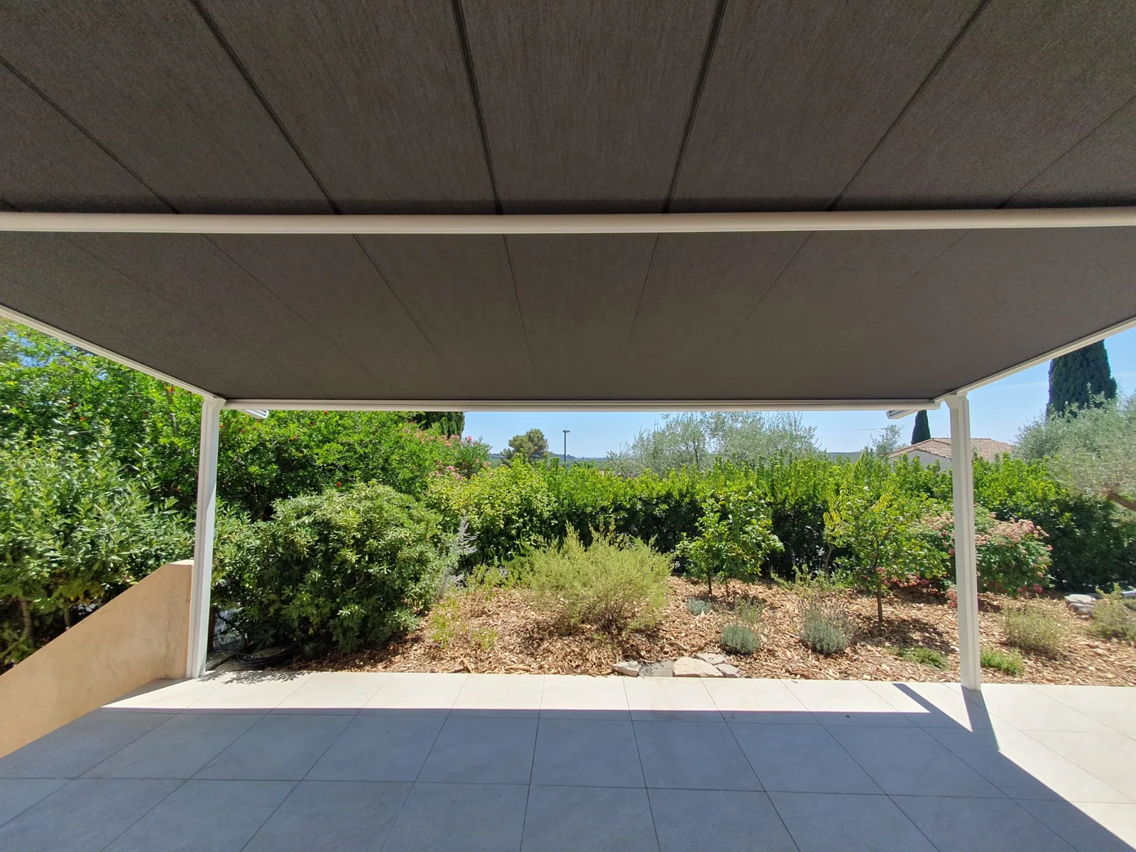 Sous la pergola déployée, vue dégagée sur le jardin verdoyant.