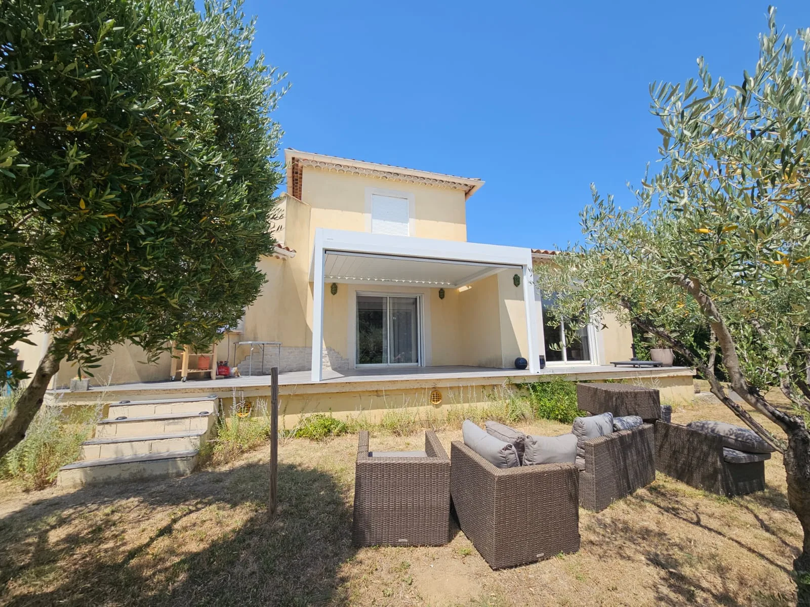 Pergola blanche et façade jaune vues du jardin planté d'oliviers