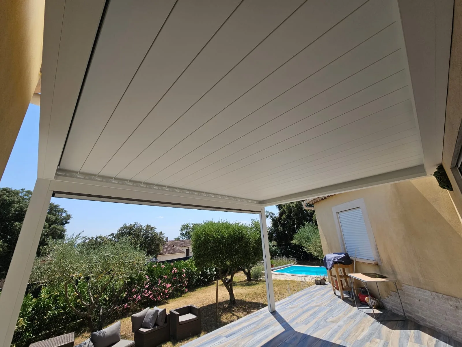 Lames orientables fermées au-dessus de la terrasse, piscine en contrebas