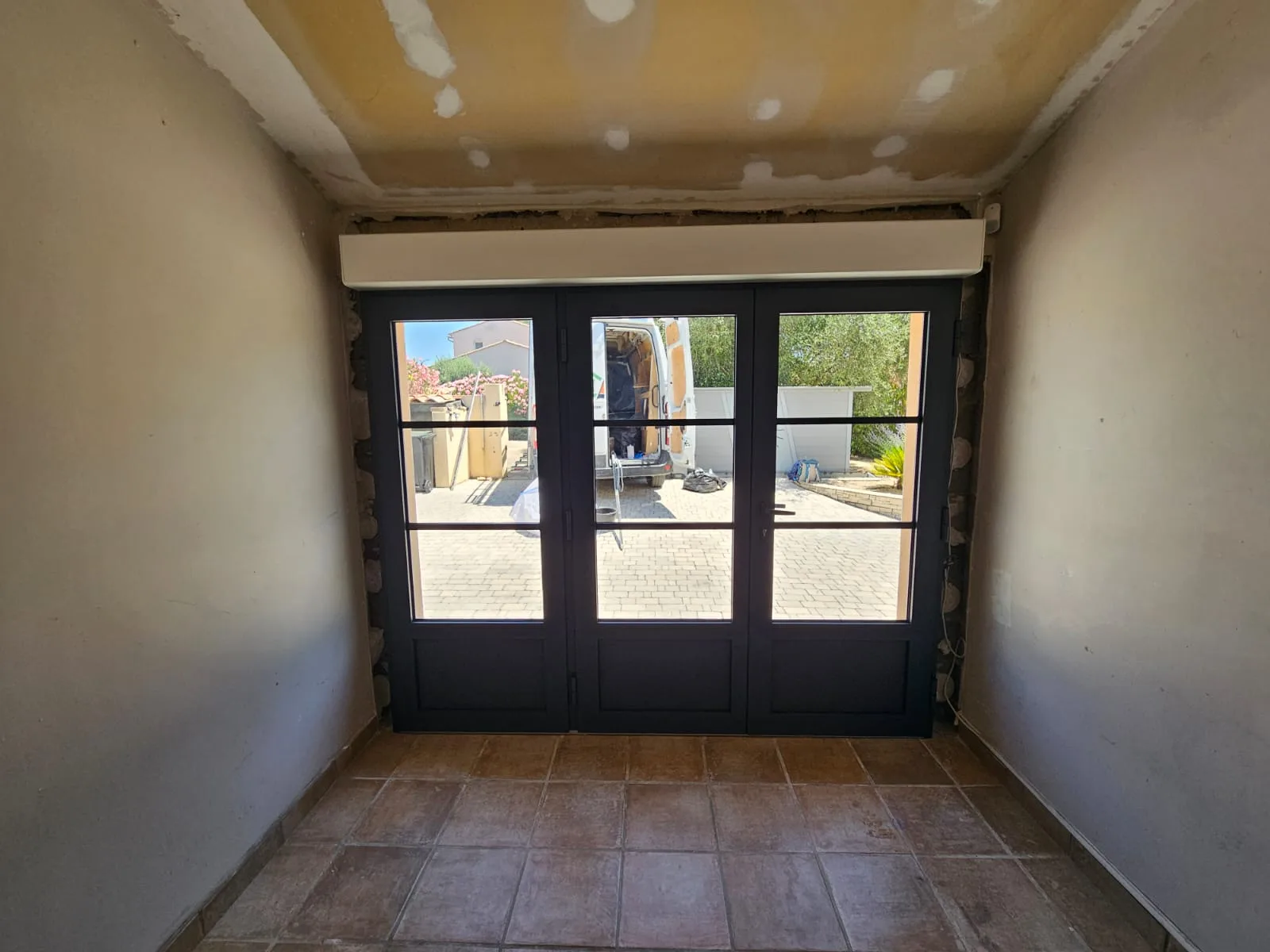 Intérieur avec nouvelle baie vitrée et volet roulant, vue sur l'extérieur.