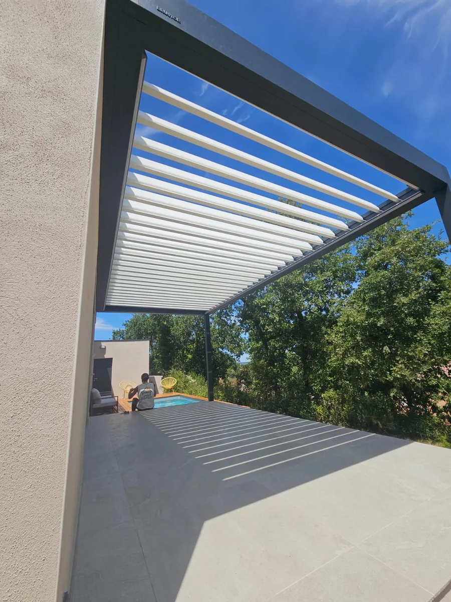 Pergola bioclimatique moderne avec structure anthracite et lames ouvertes sous ciel bleu.