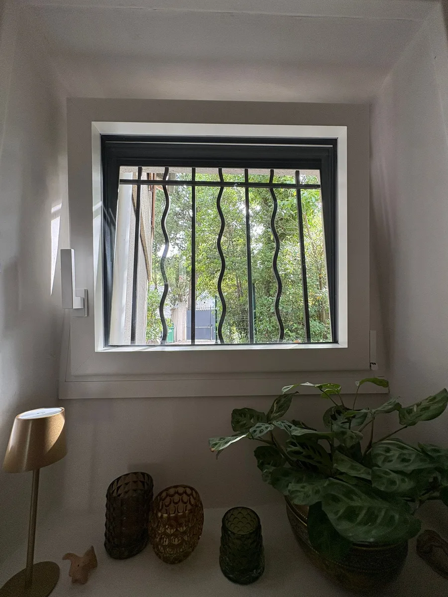 Fenêtre aluminium bicolore, intérieur blanc, barreaux de sécurité, vue verdure, Nîmes.
