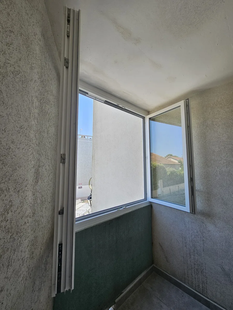 Fenêtres PVC blanches ouvertes dans un appartement nîmois, vue sur l'extérieur.