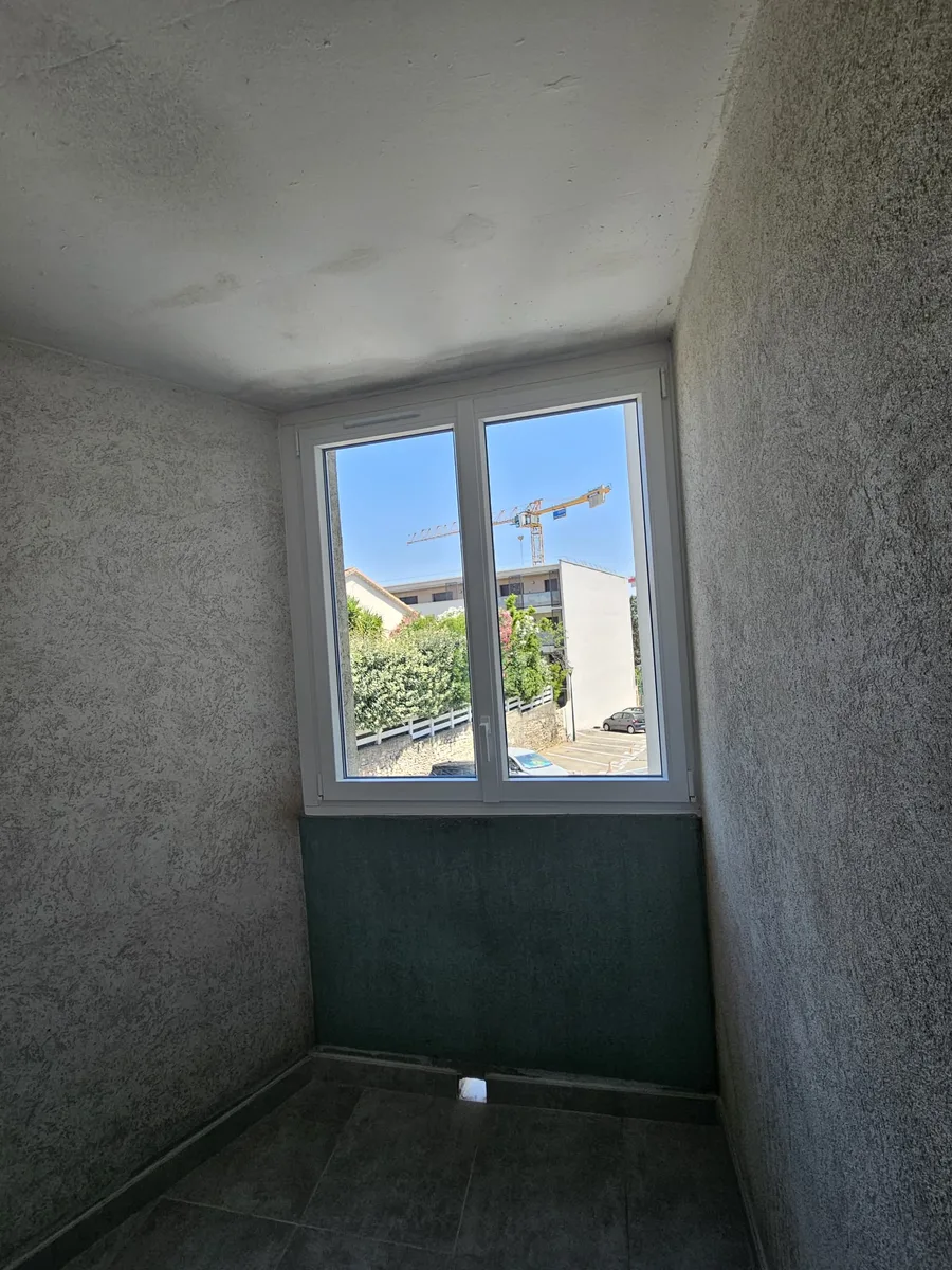 Fenêtres PVC ouvertes dans un appartement à Nîmes, vue sur grue et parking.