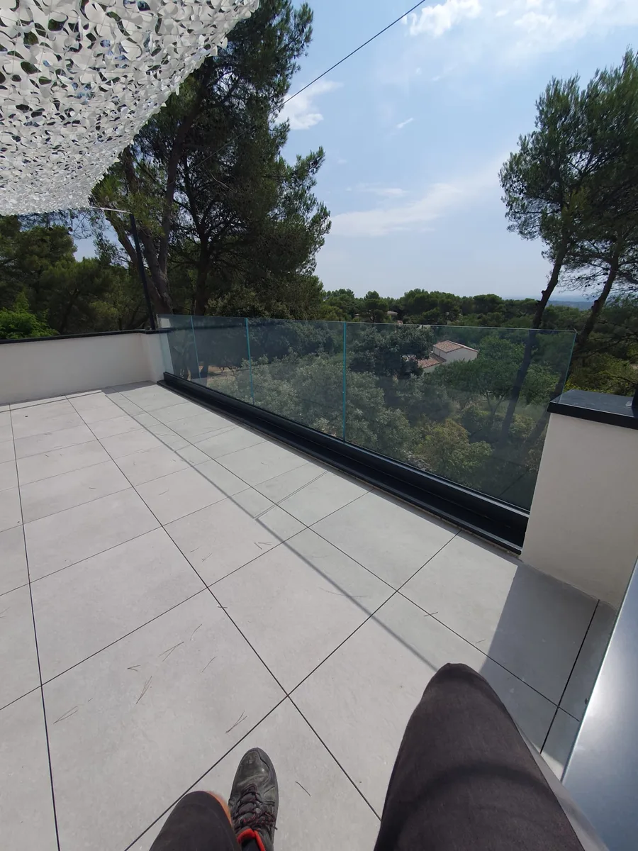 Personne sur terrasse carrelée, vue sur garde-corps en verre à Nîmes.