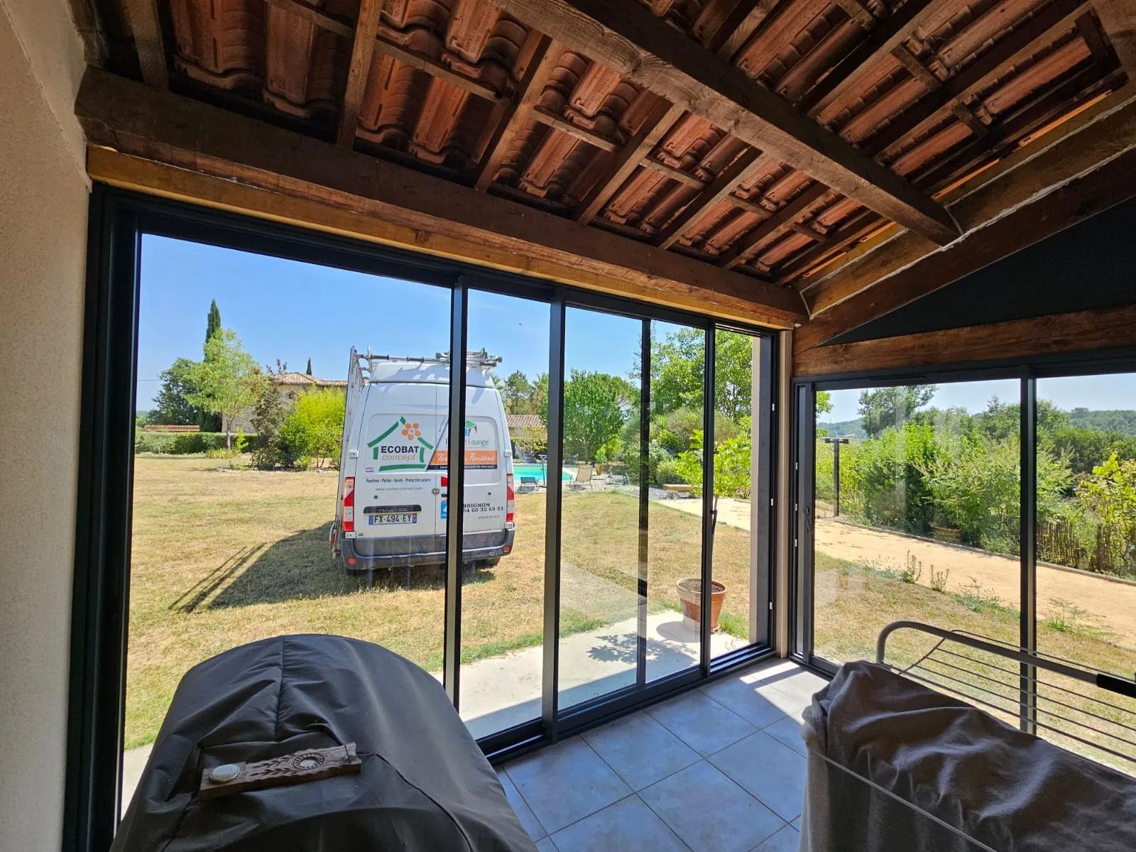 Intérieur de la véranda avec vue sur l'extérieur et le jardin ensoleillé à Saint-Cézaire-de-Gauzignan.